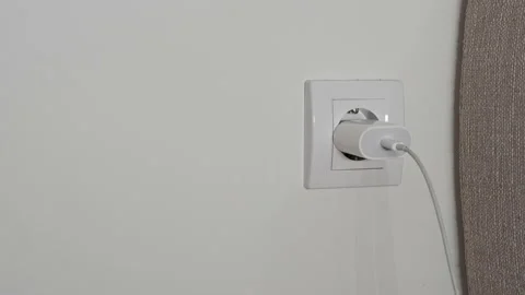 A close-up of a man's hand pulls out a white power adapter from the outlet to Stock Footage 202172624