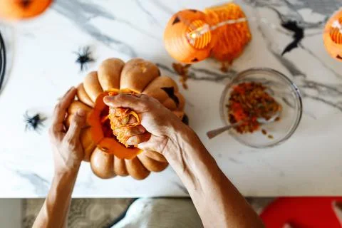 A close up of man's hand pulls seeds and fibrous material from a pumpkin before Stock Photos