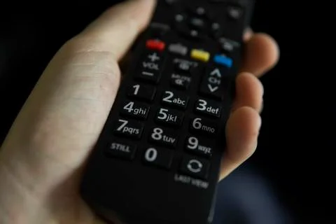Close up on a man's hand with the remote control want switch on the TV and Stock Photos