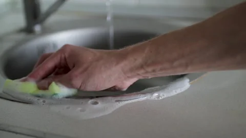 Close up of a man's hand scrubbing a stainless steel kitchen sink with a soap Stock Footage 327159266