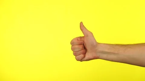 Close up of man's hand showing thumb up sign isolated on a yellow studio Stock Footage 153536469