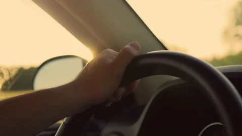 Close up of man's hand on steering wheel of car on background of sunset outside Stock Footage 201533035