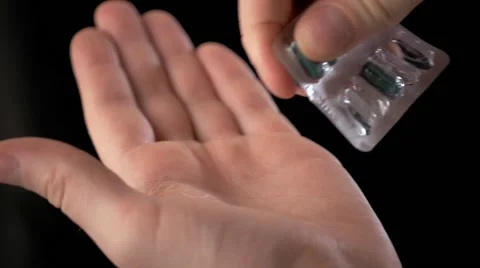 Close up of man's hand taking out pills from blister pack isolated on black Stock Footage 68721203