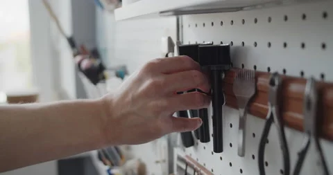 Close-up of a man's hand taking a strap end punch off a tools wall Stock Footage 146133192