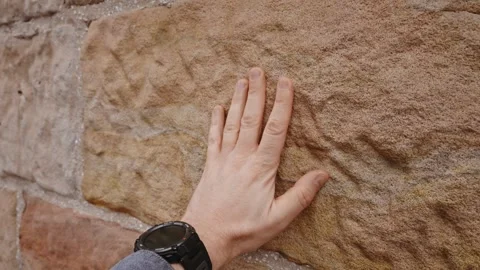 A close-up of a man's hand touching a textured stone wall. The hand is Stock Footage 307761767