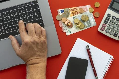 Close-up of man's hand using laptop with money and calculator on red background Stock Photos