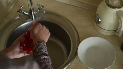 A close-up of a man's hand washing cherry tomatoes in a sink. Видео 318477027