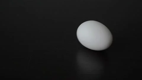 A close-up of a man's hand, which puts a white egg on a black table and begins 스톡 동영상 163516794