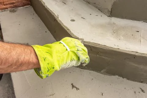 Close-up of a man's hand in work gloves leveling the surface of a step before Stock Photos