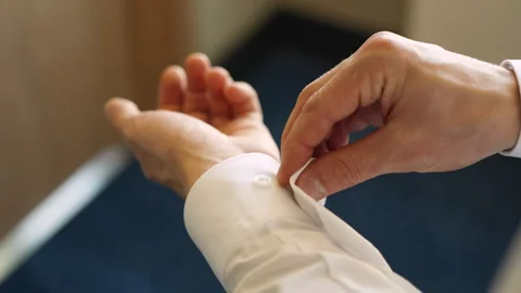 Close up of a man's hands buttoning a button on the cuff of a white shirt Stock Footage 285346476