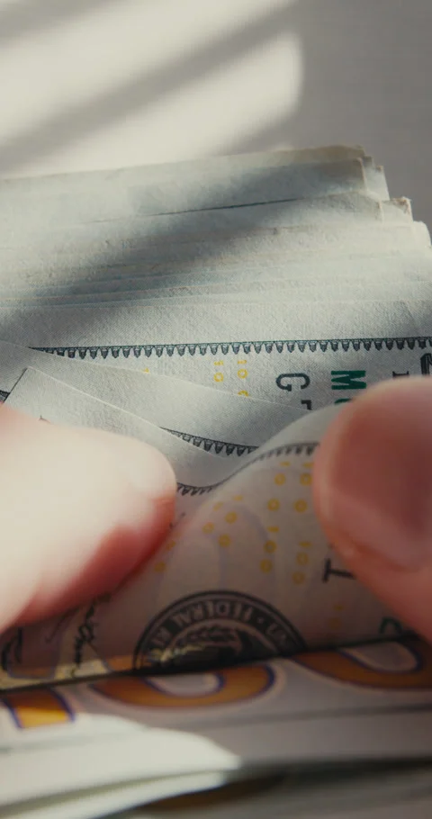 Close-up mans hands counting hundred dollar bills, soft sunlight casting striped 스톡 동영상 322720115