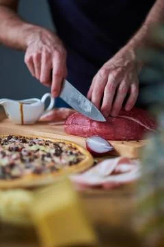 Close-up of man's hands cut beef with knife on board. Sauce-boat, half onion  Stockfoto's