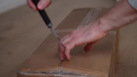 Close-up of a man's hands cutting tape with a knife to open a large box Stock Footage 291889173