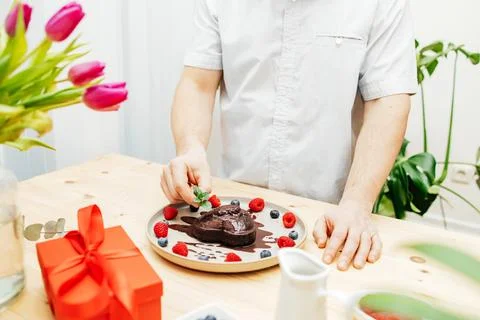 Close-up of a man's hands decorating a chocolate heart cake with a sprig of Stock Photos