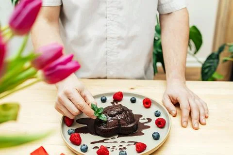 Close-up of a man's hands decorating a chocolate heart cake with a sprig of Stock Photos