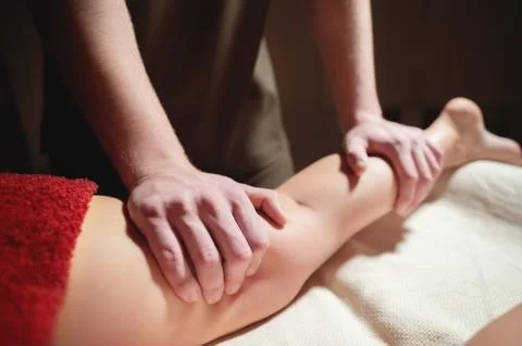 Close-up of a man's hands doing a thigh massage to a woman client in a dark room Stock Photos