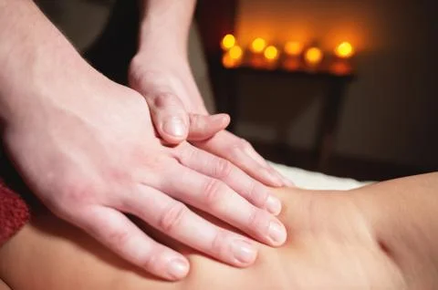 Close-up of a man's hands doing a thigh massage to a woman client in a dark room Stock Photos