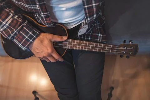 Close-up of a man's hands expertly gripping a ukulele, with one hand pressing Photos