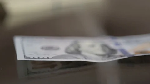 Close-up of a man's hands folding a stack of hundred-dollar bills on a glass Stock Footage 120528243