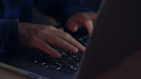 Close up of a man's hands as he types on a laptop during the evening - the Stock Footage 321392974