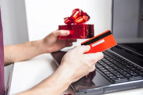 Close up of a man's hands hold a red credit card and gift near a laptop Stock Photos