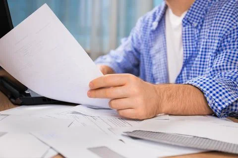 Close-up of a man's hands holding a document at a desk cluttered with envel.. Stock Photos