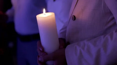 Close-up of a mans hands holding a large, thick white candle. The scene is Stock Footage 322183828