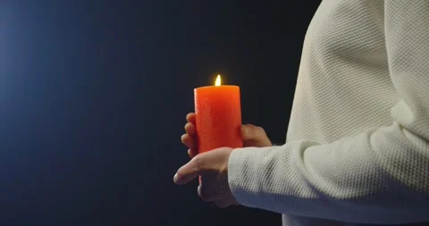 Close-up of man's hands holding a red burning candle against a blue background. Stock Footage 305060314