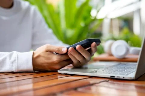 Close up of man's hands holding using phone over laptop while sitting outdo.. Foto stock