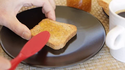 Close up of man's hands that puts jam on a slice of biscuit or rusk Stock Footage 128465611