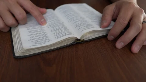 A close up of a man's hands reading the bible on a dark wooden table Stock Footage 102446212