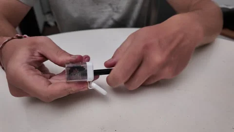 Close up of a mans hands sharpening a pencil with a sharpener above a table Stock Footage 318339151