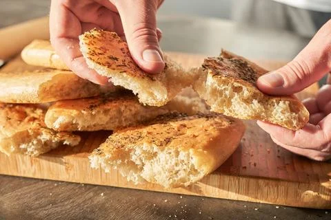 Close-up of a man's hands taking slices of bread from a wooden board. Stock Photos