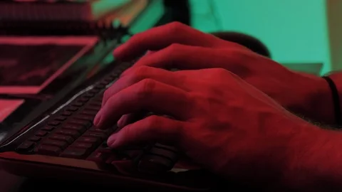 Close up of man's hands typing on a keyboard in a green and red room Stock Footage 118977193