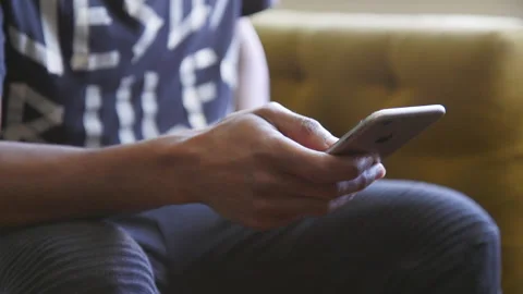Close up of a man's hands using an iPhone while sitting on a couch. Stock Footage 143518711