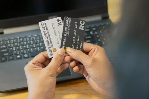 Close-up man's hands using laptop and holding black and white credit carsds. Stock Photos