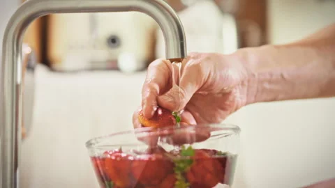 A close-up of a mans hands washing a ripe strawberry under running water in Stock Footage 337937646