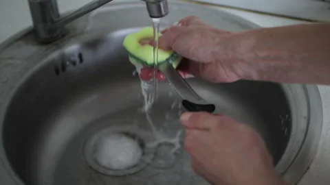 Close-up of a man's hands washing a sharp kitchen knife with a sponge and soap Stock Footage 327159237