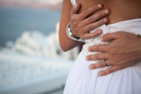 Close-up of mans hands with a wedding ring hugging the back of a woman agains Stock Photos