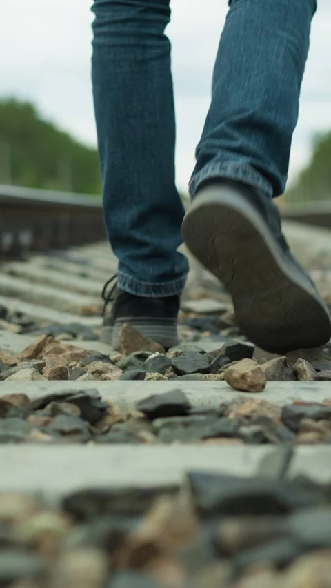 Close-Up of Mans Legs Walking Alone on Rocky Railway Tracks Surrounded by Trees Video stock 316506445
