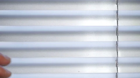 Close up mans shaking hand moves towards closed Venetian blinds and opens slats Vidéo 128640252