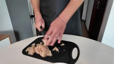 Close up of manually slicing raw chicken fillet with a kitchen knife on a Stock Footage 330058294
