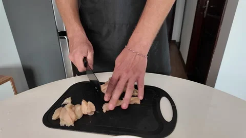 Close-up of manually slicing raw chicken fillet with a kitchen knife on a board 스톡 동영상 331138717