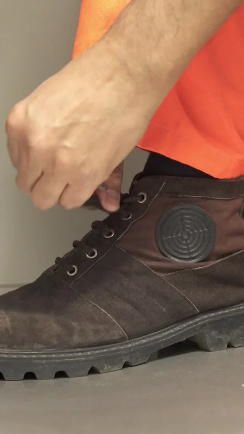 Close-up of a manufacturing worker's hands tying the laces on his work boots Видео 337033826