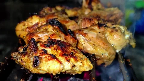 A close-up of marinated chicken pieces grilled over glowing embers.4K Stock Footage 339044125