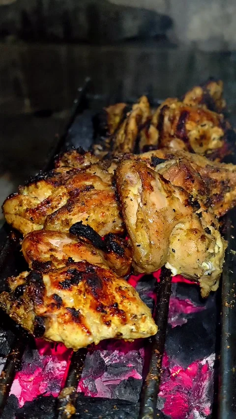 A close-up of marinated chicken pieces grilled over glowing embers.4K Stock Footage 339044128