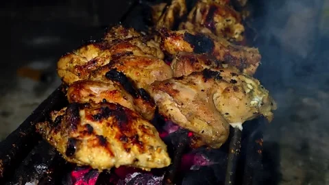 A close-up of marinated chicken pieces grilled over glowing embers.4K Stock Footage 339044144