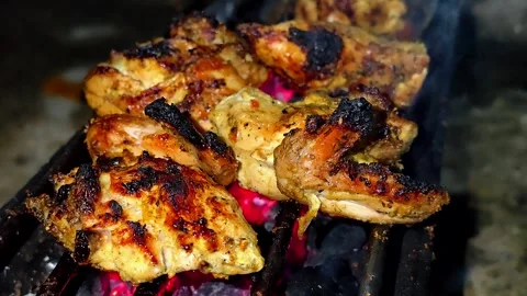 A close-up of marinated chicken pieces grilled over glowing embers.4K Stock Footage 339044145
