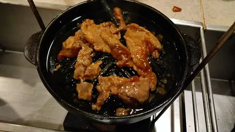 Close-up of marinated meat grilling in a small black cast iron pan Stock Footage 345640698