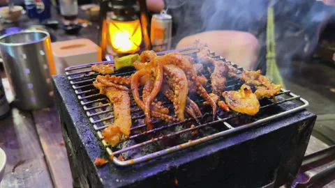 Close-up of marinated octopus tentacles and meat sizzling on a tabletop Vidéo 333678084